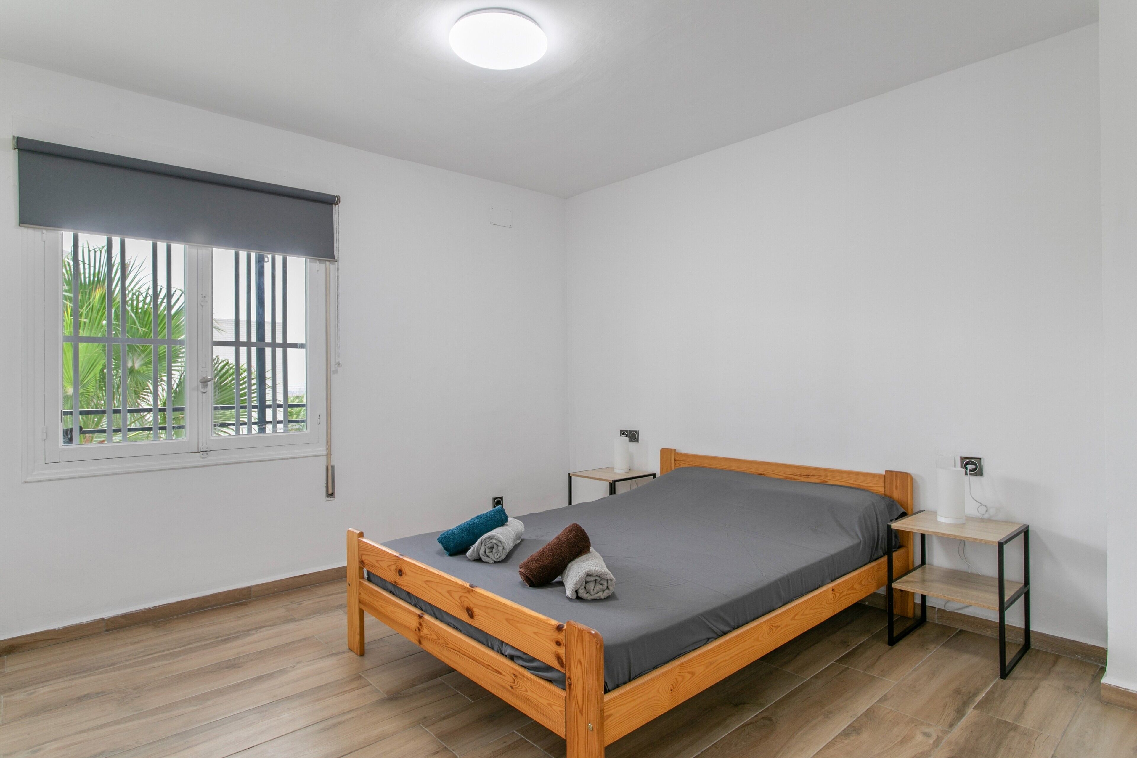 A single-bed room with a wooden frame, grey mattress, and two bedside tables with lamps.