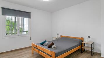 A single-bed room with a wooden frame, grey mattress, and two bedside tables with lamps.