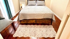 Ein Schlafzimmer mit Bett, Deckenventilator, Fenster mit Vorhängen und Holzboden.