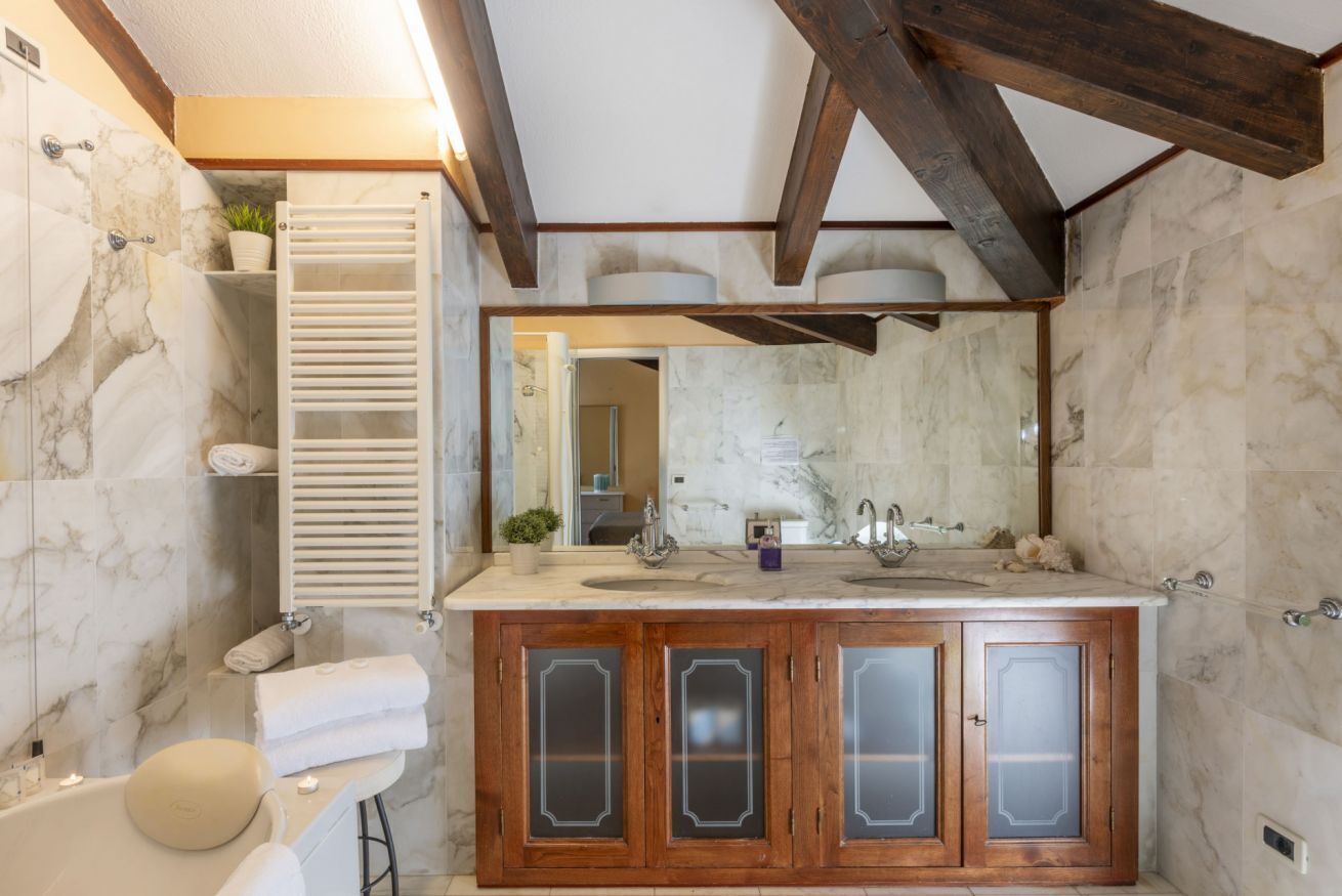 Een badkamer met marmeren wanden, een houten wastafelmeubel met ruiten van geëtst glas, een badkuip en een handdoekrek.