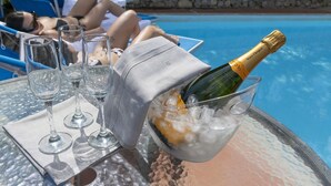 Escena junto a la piscina con una mesa, una botella de champán y copas de vino vacías.