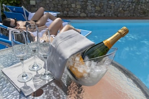Une scène au bord de la piscine, avec une table, une bouteille de champagne et des verres à vin vides.