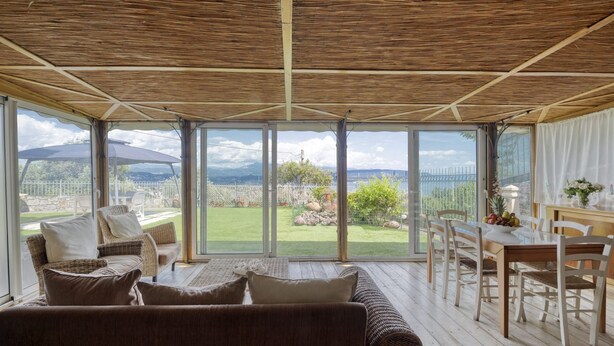 Una habitación amplia con un gran ventanal que da a un jardín, mobiliario de mimbre y techo de madera.