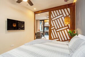 Een slaapkamer met een bed, een aan de muur bevestigde televisie, een plafondventilator en een houten scheidingswand met een hanglamp.
