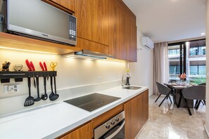A modern kitchen with wooden cabinets, a microwave, a built-in oven, and a dining area with a table and chairs. - Great studio, close to the supermarket, Fifth Avenue, and the beach. (Playa del Carmen)