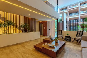 Een moderne lobby met een houten receptiebalie, zithoek en een trap.