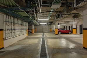 A parking garage with a red car, concrete floors, and overhead pipes. - Great studio, close to the supermarket, Fifth Avenue, and the beach. (Playa del Carmen)