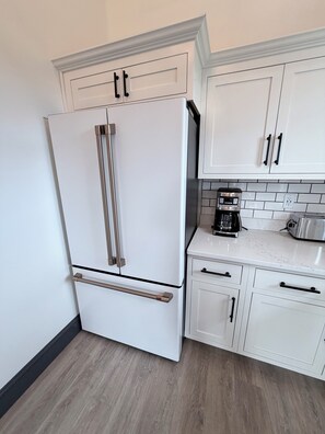 A kitchen with white cabinetry, a stainless steel refrigerator, a coffee maker, and a toaster.
