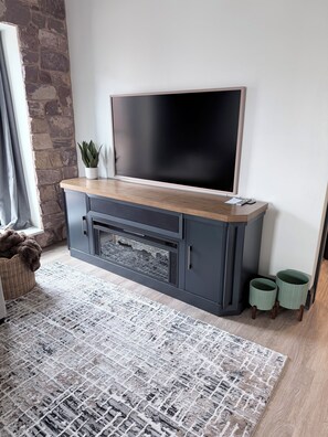 A modern living room with a flat-screen TV mounted on a grey cabinet, a patterned rug, and a stone accent wall. - 2-bedroom/2-bath Condo in the Heart of Marquette on the Shores of Lake Superior (Marquette)
