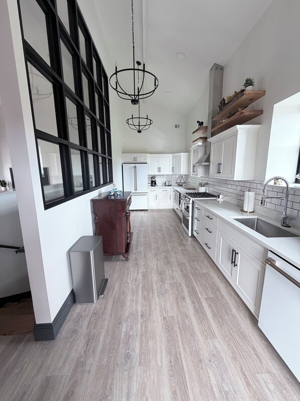 Una cocina moderna con armarios blancos, un refrigerador de acero inoxidable y una mesa de comedor de madera.