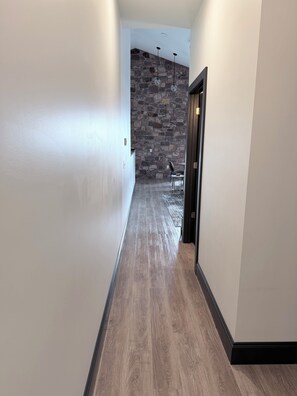 A hallway with a wooden floor, a stone wall, and a door leading to a room.
