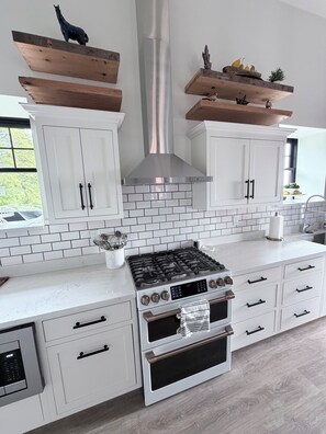 A modern kitchen with white cabinetry, a stainless steel range hood, and a gas stove. - 2-bedroom/2-bath Condo in the Heart of Marquette on the Shores of Lake Superior (Marquette)