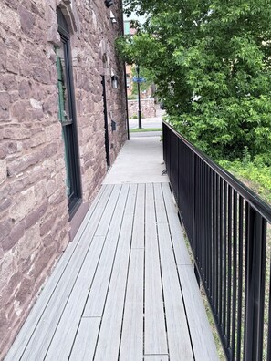 A wooden walkway with a stone building on one side and a metal fence on the other.
