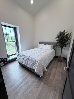 A bedroom with a bed, a window, a potted plant, and a door. - 2-bedroom/2-bath Condo in the Heart of Marquette on the Shores of Lake Superior (Marquette)