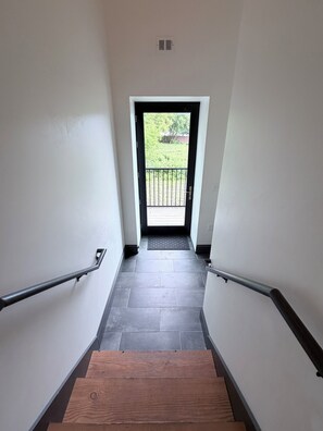 A staircase with a wooden finish, leading to a door with a black frame and a view of a green outdoor area. - 2-bedroom/2-bath Condo in the Heart of Marquette on the Shores of Lake Superior (Marquette)