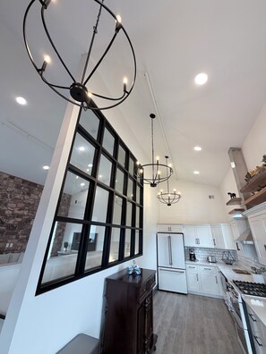 A modern kitchen with white cabinets, a large window, and pendant lighting.