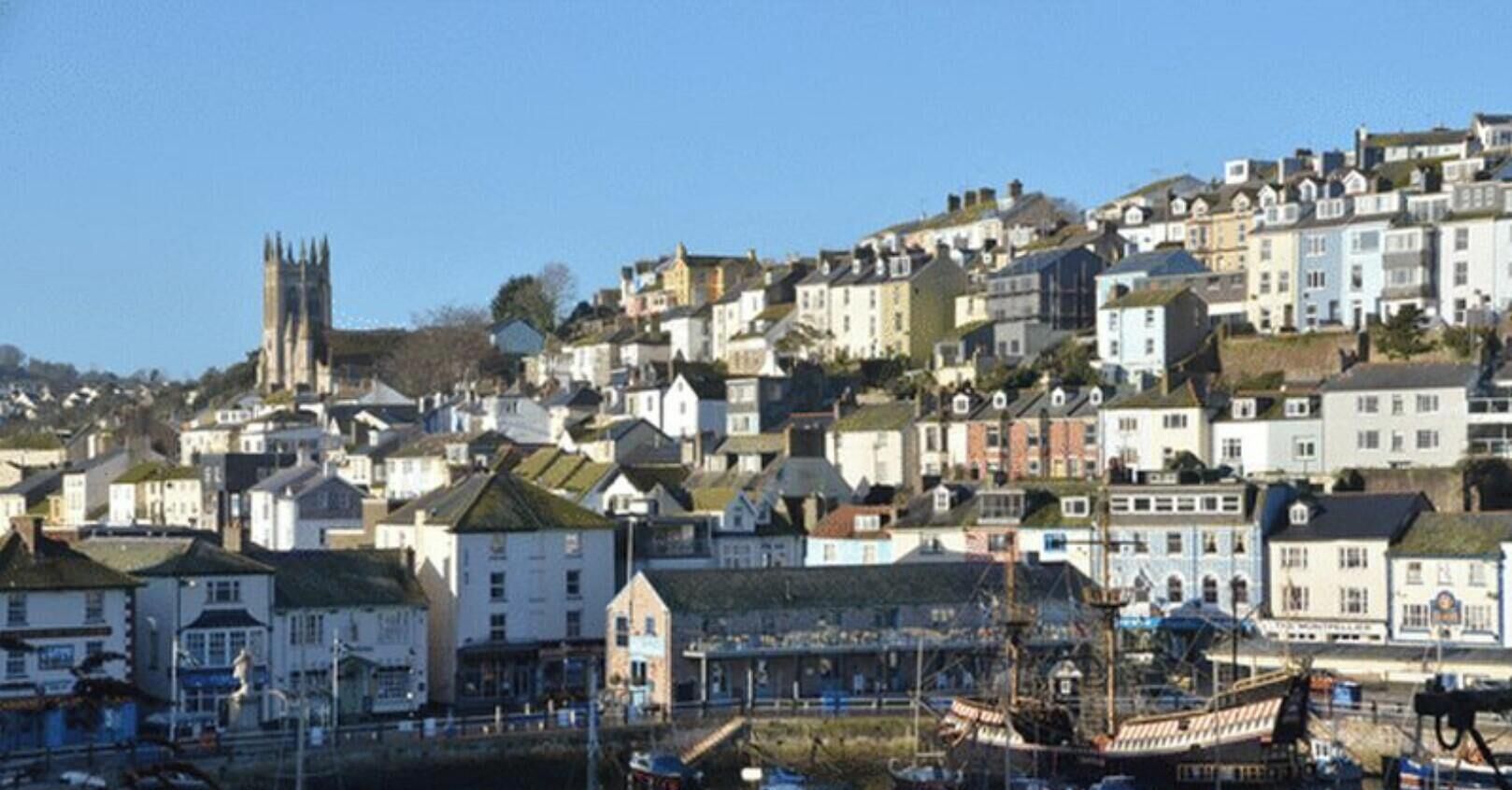 A coastal town with a prominent church tower, residential buildings, and a waterfront area with boats.