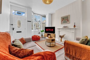 Een woonkamer met een bank, een rode relaxfauteuil, een salontafel, een open haard en een televisie waarop 'NETFLIX' staat.