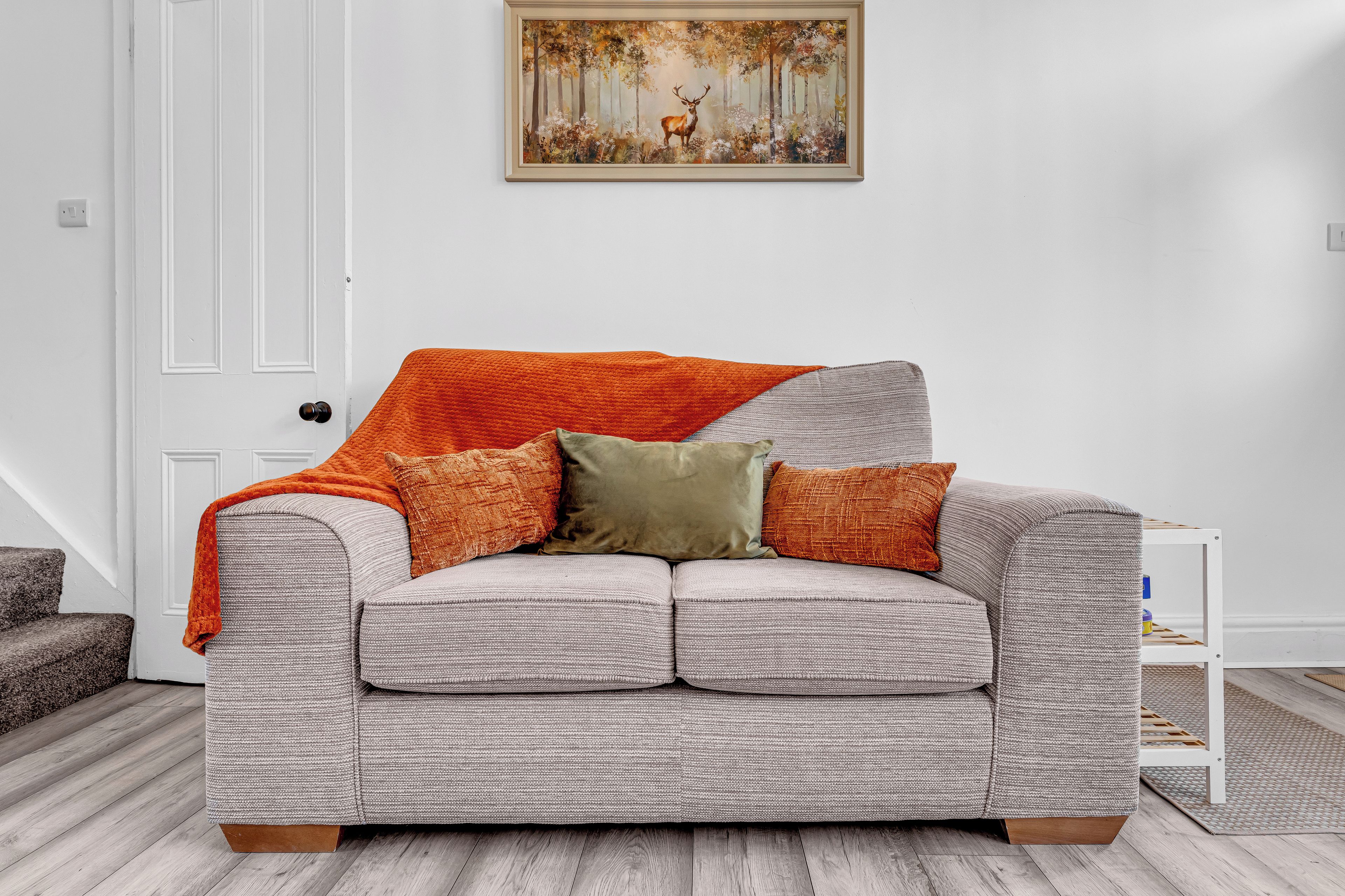 A grey upholstered sofa with a textured fabric, two orange throw pillows, and a green pillow.