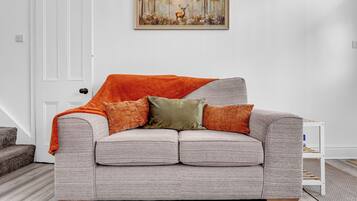 A grey upholstered sofa with a textured fabric, two orange throw pillows, and a green pillow.