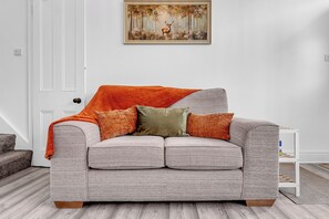 Un canapé gris recouvert d’un tissu texturé, agrémenté de deux coussins décoratifs orange et d’un coussin vert.