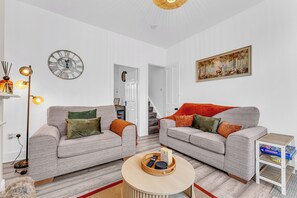 Una sala de estar moderna con dos sofás, una mesa de centro, un reloj de pared y un cuadro.