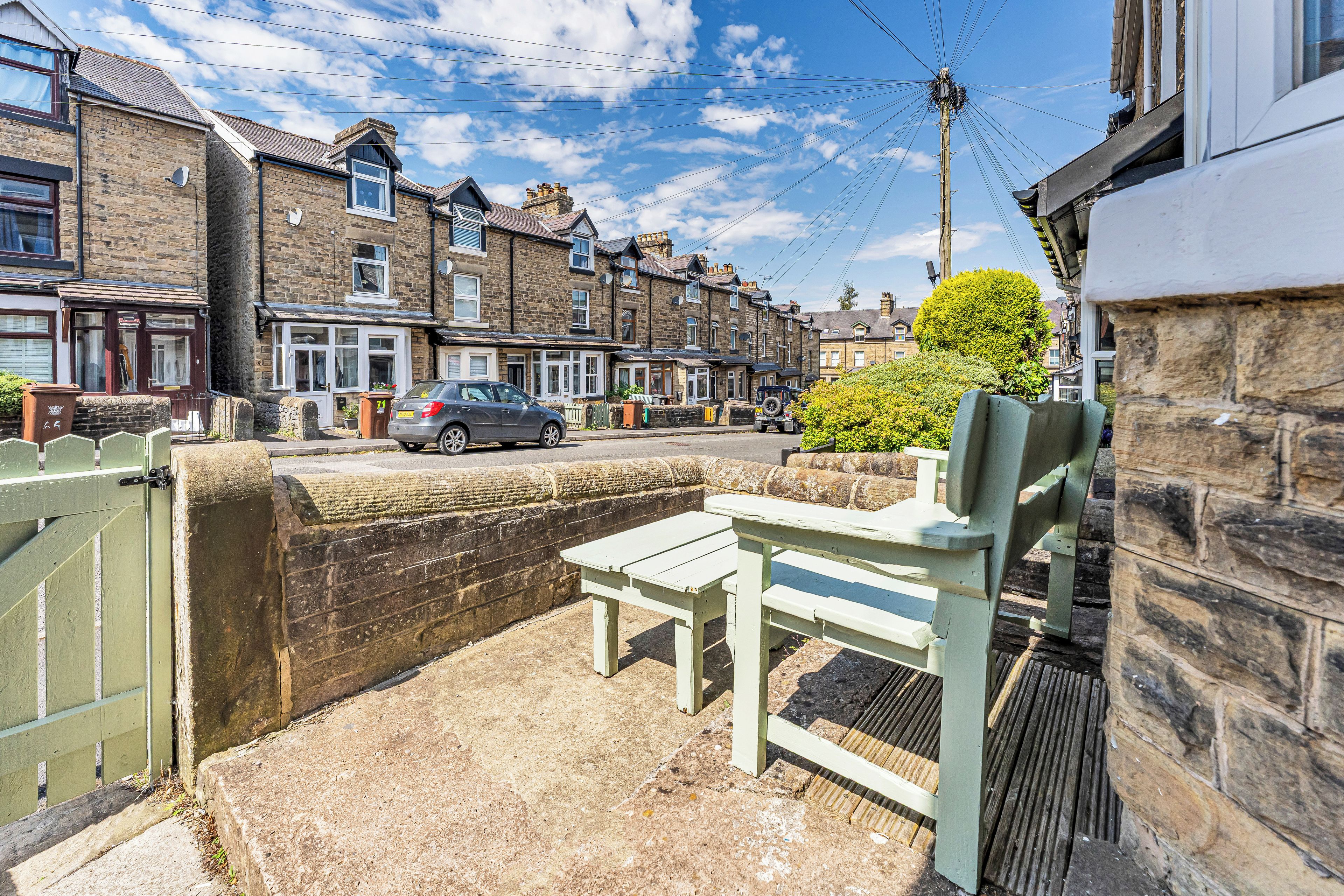 A residential street with houses, a parked car, and a bench.