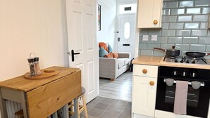 A kitchen with a stove, oven, and a dining area with a wooden table and chairs. - Peak Side Terrace, 3BR, Sleeps 5 - Buxton (Buxton)