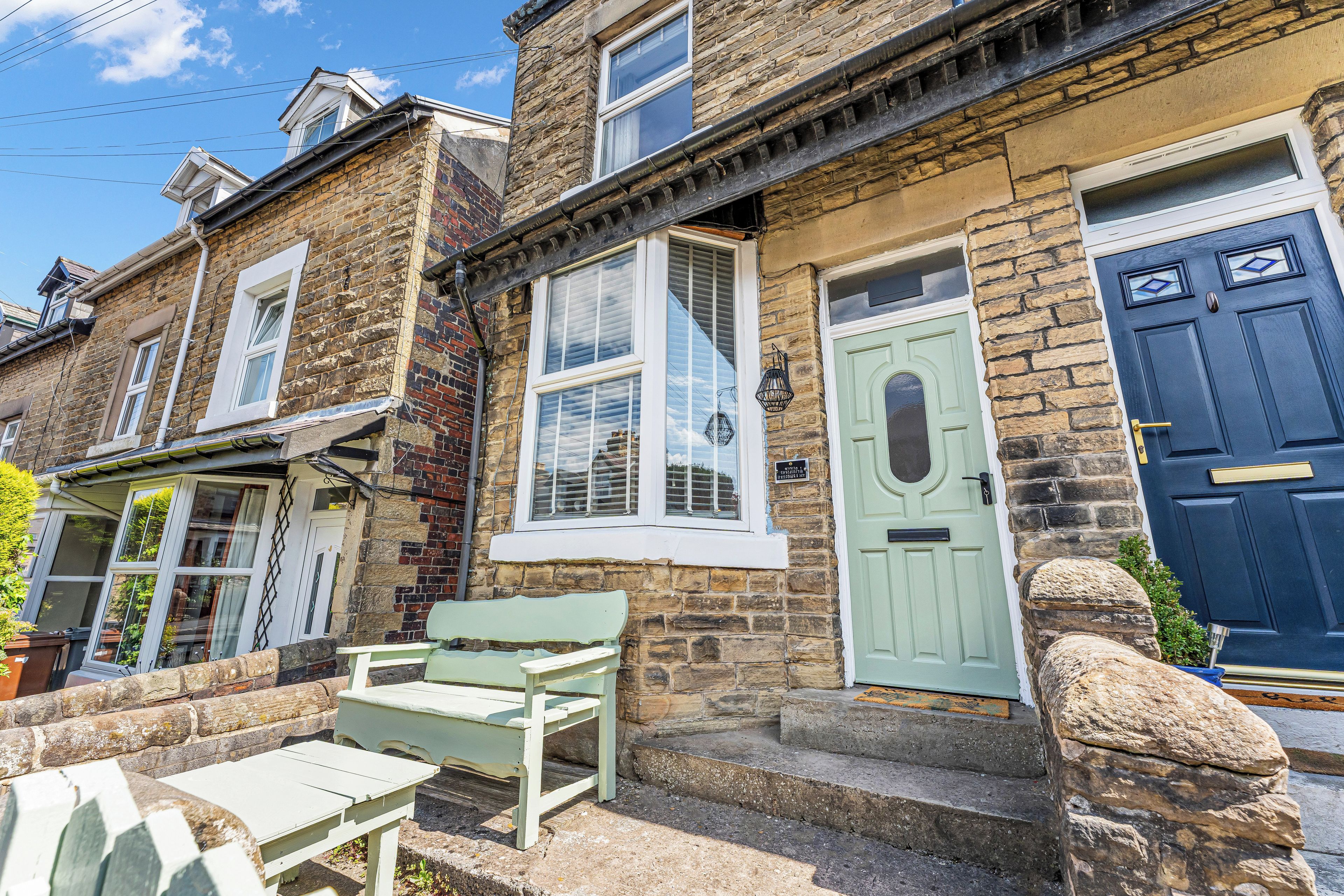 A traditional stone house with a green door, white window frames, and a bench outside.