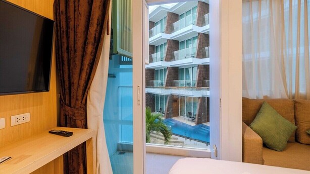 Habitación de hotel con televisión, cama, sofá, ventana con vista a un edificio y una piscina.