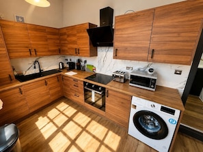 Eine moderne Küche mit Holzausstattung, einem Einbauofen, einer Mikrowelle, einem Toaster und einer Waschmaschine.