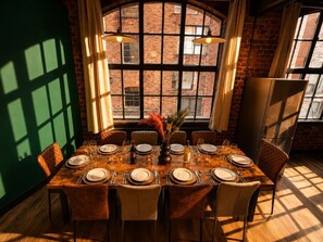 Un coin repas avec un mur en briques, de grandes fenêtres et une table dressée pour six personnes.
