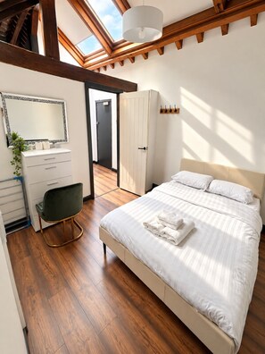 Un dormitorio con cama, tocador con espejo, una silla y un armario.
