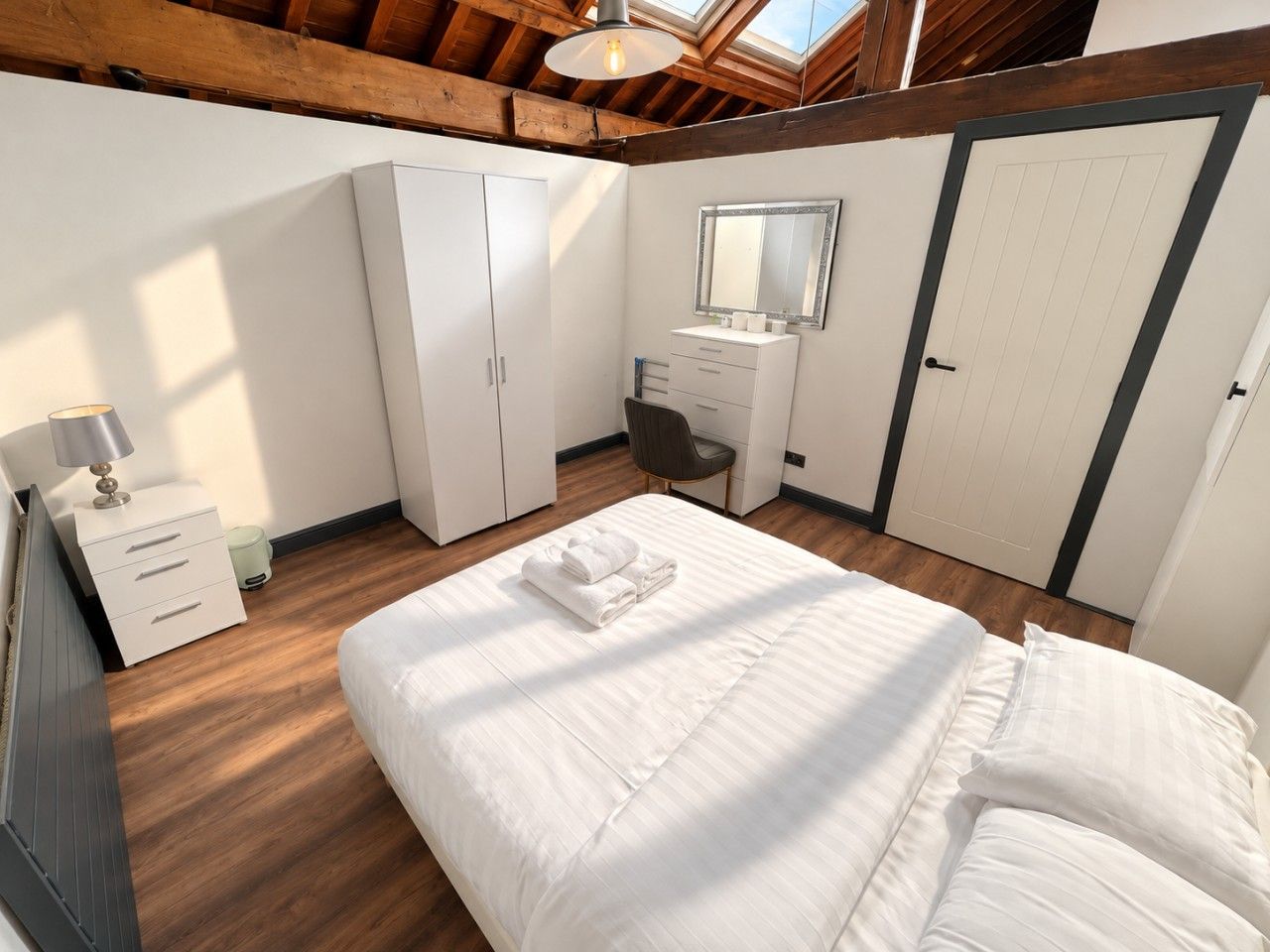 Ein Schlafzimmer mit einem großen Bett, einem Kleiderschrank, einem Schreibtisch und einem Spiegel.