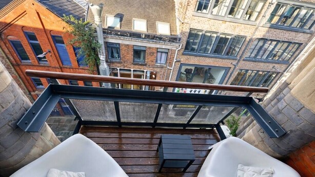 A balcony with two white cushioned chairs, a small table, and a metal railing.