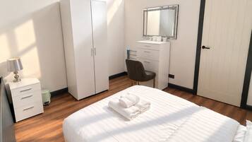 A bedroom with a skylight, a bed with white linens, a desk with a mirror, and a wardrobe.