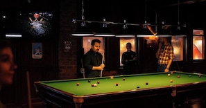 A pool table with balls, a person playing, and another person standing by.