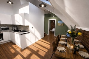 A modern kitchen with white cabinets and a dining area with a wooden table set for four. - City Centre | Bars & Shops | Free Parking (Merseyside)