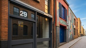 Straßenansicht mit einem Gebäude mit der Nummer 29, einem Laden mit einer blauen Tür und einem farbenfrohen Wandgemälde am Nachbarhaus.