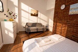 A bedroom with a bed, a sofa, a dresser, a clock, and a painting on the wall. - City Centre | Sleeps 6 | Bars, Parking & Netflix (Merseyside)