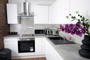 A modern kitchen with white cabinets, stainless steel appliances, a brick wall, and a potted orchid. - City Centre | Sleeps 6 | Bars, Parking & Netflix (Merseyside)