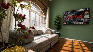 Ein gemütliches Wohnzimmer mit einer Couch, einer Topfpflanze und einem an der Wand befestigten Fernseher, der eine Netflix-Auswahl zeigt.