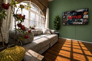 A cozy living room with a sofa, a potted plant, and a wall-mounted TV displaying a Netflix collection. - City Centre | Sleeps 6 | Bars, Parking & Netflix (Merseyside)