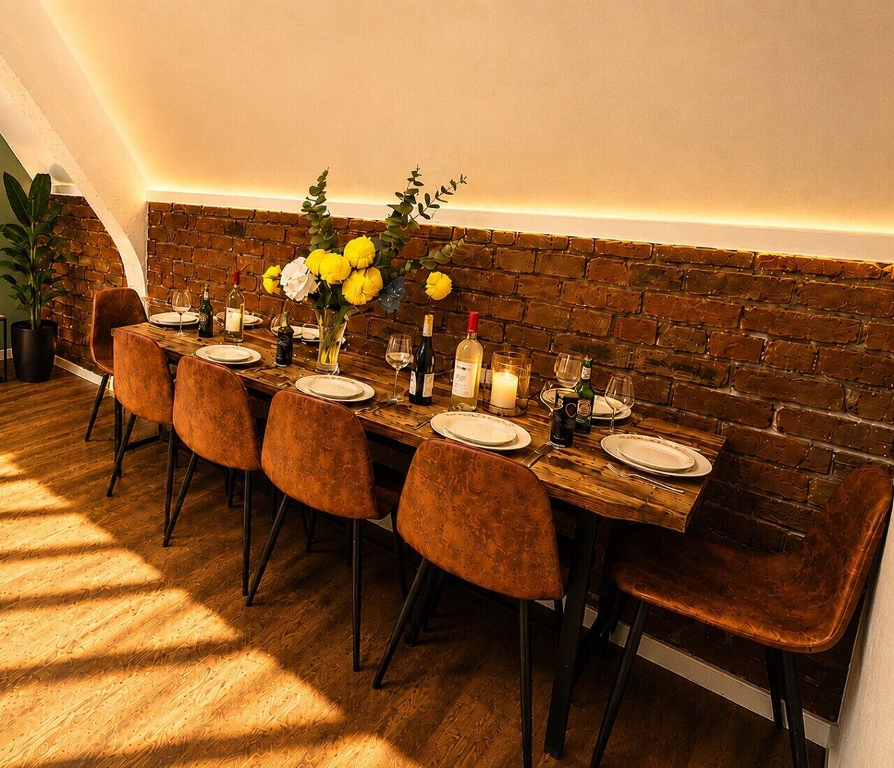 A dining table set with chairs, a brick wall, and a potted plant.