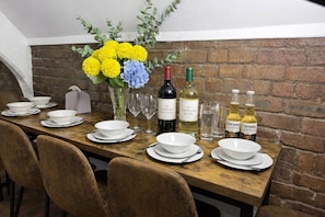 A dining table set with white plates, bowls, and wine bottles, including Sauvignon Blanc and Corona, against a brick wall backdrop. - City Centre | Sleeps 6 | Bars, Parking & Netflix (Merseyside)