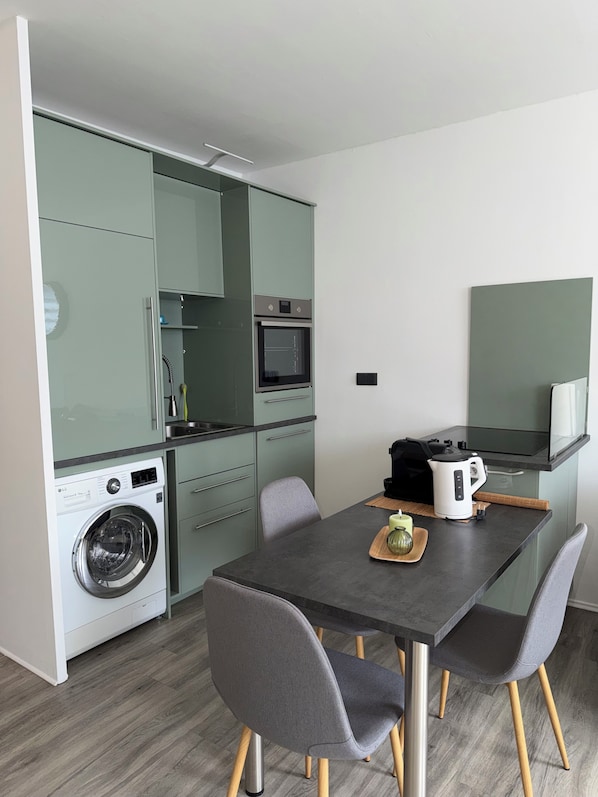 Cocina compacta con lavadora, microondas y comedor con mesa y sillas.