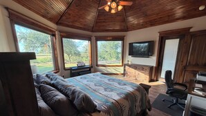 Ein Schlafzimmer mit einem Bett, einem Schreibtisch, einem Sessel, einem Fernseher und großen Fenstern.