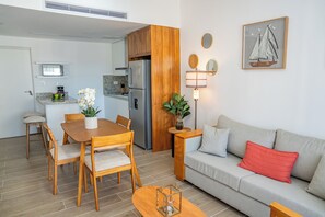 Moderni keittiö, jossa on jääkaappi, mikroaaltouuni ja liesi. Ruokailutilassa on pöytä ja tuolit, ja olohuoneessa on sohva ja lamppu.