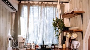Una cuina amb cafetera, planta penjant i estant amb tasses.