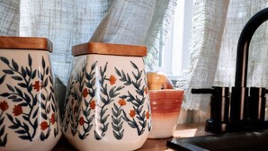Dos recipients de ceràmica amb motius florals sobre una superfície de fusta prop d'una finestra amb cortines translúcides.